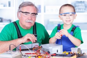 a man and his grandson tinkering with electronics while wearing safety goggles